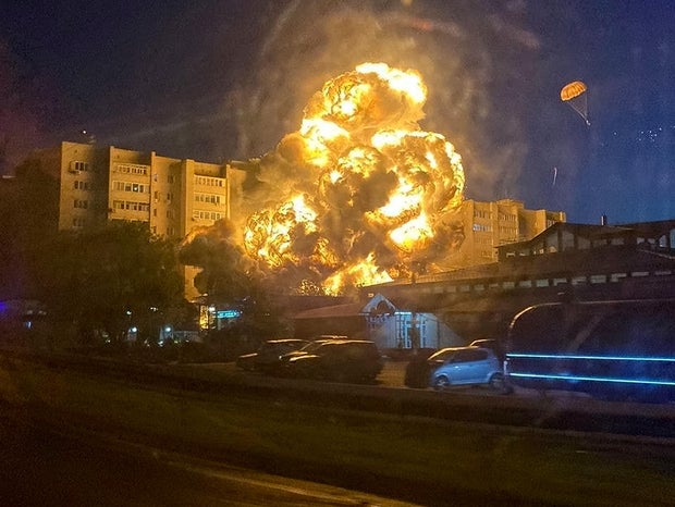 In this handout photo released by Kooperativ Telegram Channel, flames and smoke rise from the scene after a warplane crashed into a residential area in Yeysk, Russia, Oct. 17, 2022. One of the pilots, right, descends on a parachute. 