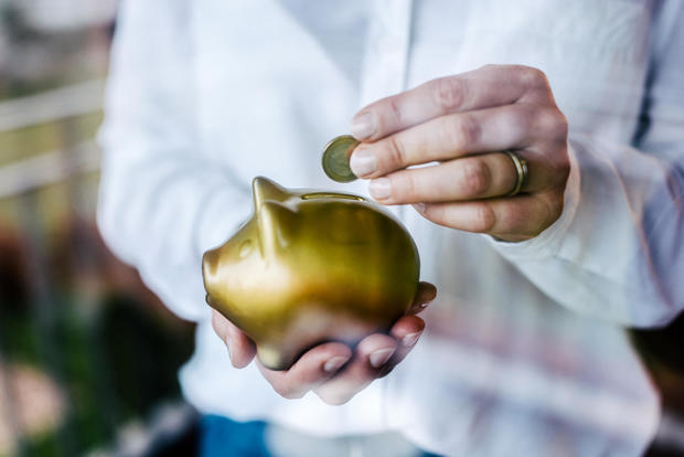 Woman putting savings in a golden piggy bank while standing in front of a window. 