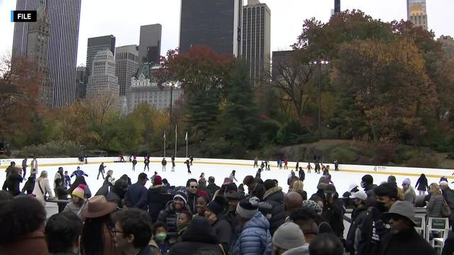 Dozens of people crowd around Wollman Rink in Central Park as others skate on the ice. 