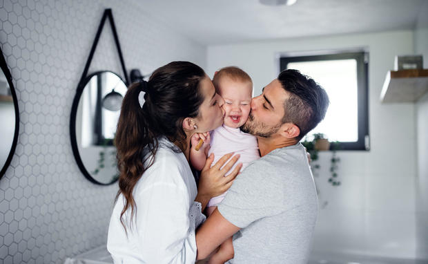 Portrait of young couple with toddler girl in the morning indoors in bathroom at home, kissing. 