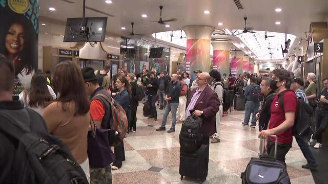 A crowd of people stands inside Penn Station. 
