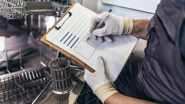 Male Technician Sitting Near Dishwasher Writing On Clipboard In Kitchen 