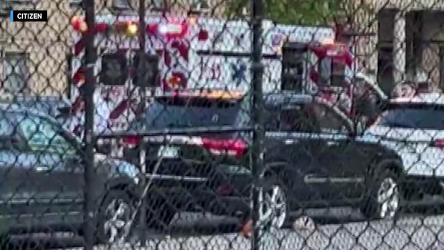 An ambulance sits parked on a street outside a playground. 