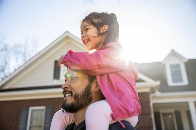 Daughter on father's shoulders in front of suburban home 