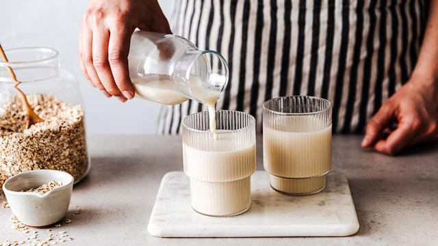 Close-up of a woman pouring oat milk in glasses 