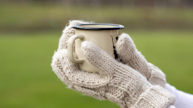 Hands of young woman wearing gloves holding coffee mug outdoors 