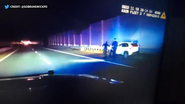 Dash cam video shows two police officers walking alongside a moving vehicle on a highway at night. 