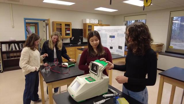 Four students stand in a high school science lab. 