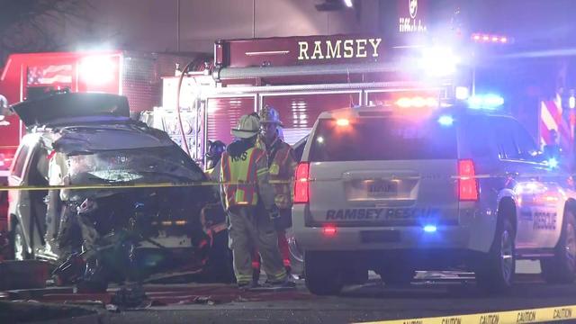 Emergency responders stand near a damaged vehicle behind crime scene tape. 
