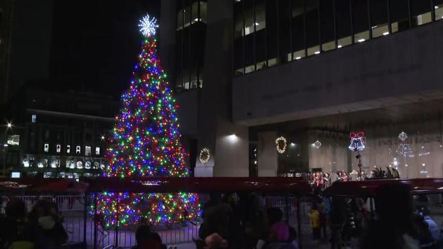 A small train drives by a lit Christmas tree outside the Adam Clayton Powell Jr. state office building. 