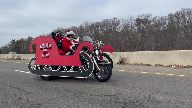 A motorcyclist dressed as Santa Claus drives a motorcycle that has been outfitted to look like a sleigh. 