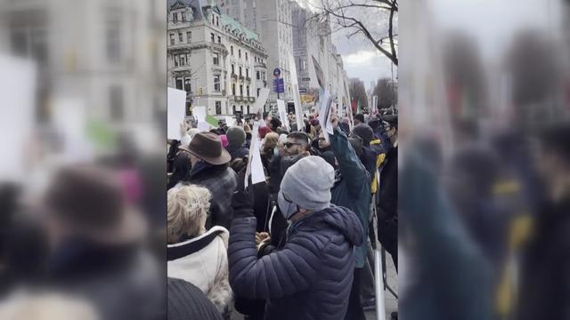 Crowds of people, some holding signs, stand in front of the home of the Iranian ambassador to the United Nations. 