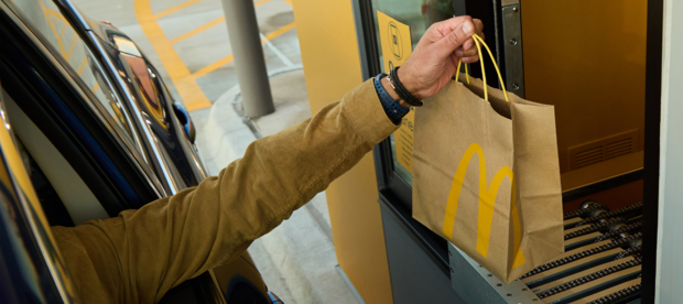Hand holding McDonald's bag above conveyor belt 