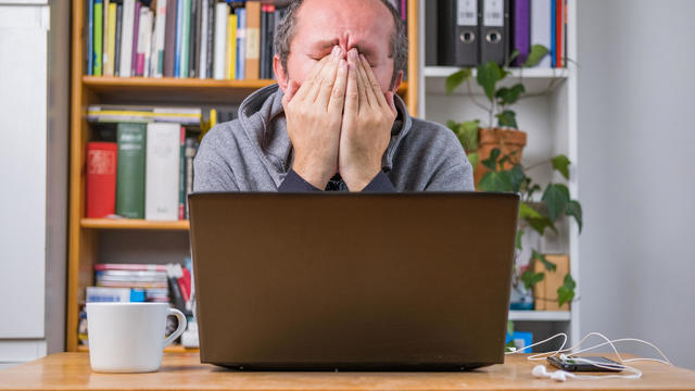 Frustrated man, working online from home office on computer laptop behind vintage desk 