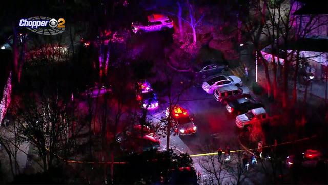 An aerial view of an apartment building. The parking lot is blocked off by crime scene tape and police and EMS vehicles are parked outside. 