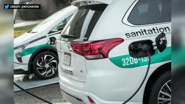 Two electric New York City sanitation vehicles sit parked at charging stations. 