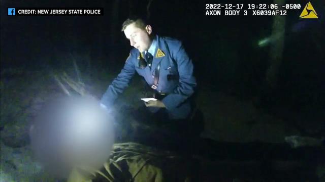 Body cam footage shows a New Jersey state trooper kneeling on the ground of a forest next to a man. 