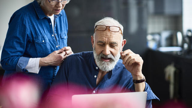 Hipster senior man with beard using laptop and woman watching 