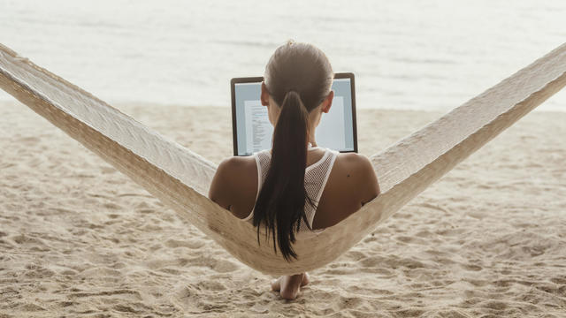 Rear view of woman using laptop computer while relaxing on hammock 