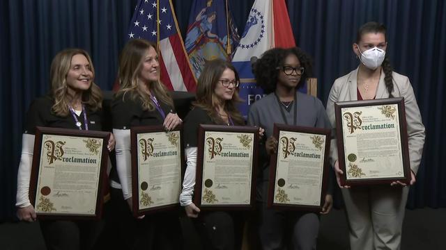 Five school nurses stand in a row holding proclamations. 