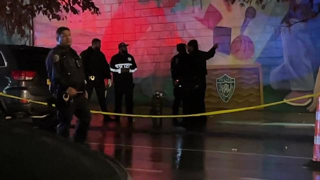 Police officers stand behind crime scene tape outside a Police Athletic League building. 