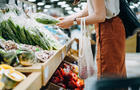 Cropped shot of young Asian woman shopping for fresh organic groceries in supermarket. She is shopping with a cotton mesh eco bag and carries a variety of fruits and vegetables. Zero waste concept 