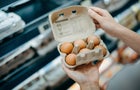 Close up of young Asian woman grocery shopping in a supermarket. She is holding a box of fresh organic free range eggs in front of a refrigerated section. Healthy eating lifestyle 
