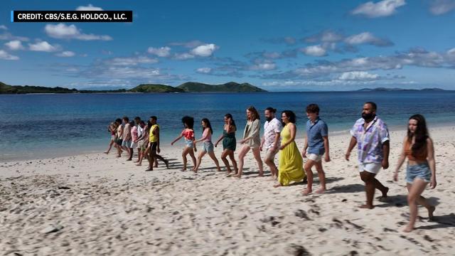 The 18 castaways from "Survivor 44" walk down a beach. 