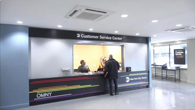 A individual stands at the window of an MTA Customer Service Center to talk to two employees. 