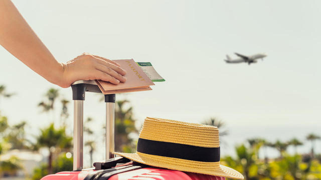 Woman with pink suitcase and passport with boarding pass standing on passengers ladder of airplane opposite sea with palm trees. Tourism concept 