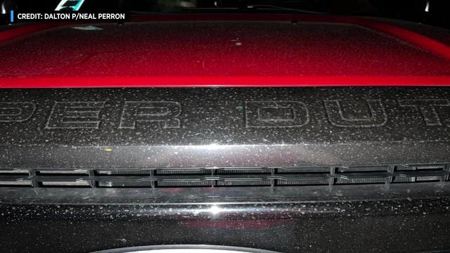 A soot-like residue can be seen on the hood of a vehicle. 