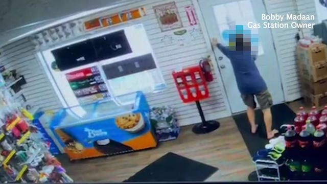 A woman wearing shorts and a long-sleeved shirt with no shoes on holds a gas station door closed. 
