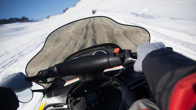 Person Riding Snowmobile On Snowy Field 