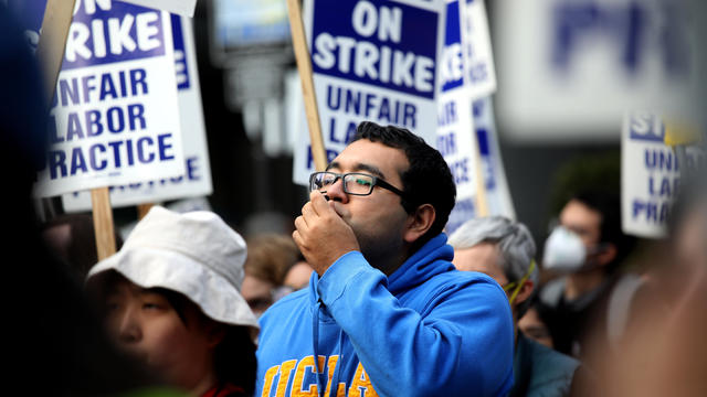 Man in UCLA shirt and glasses amid a crowd of "UAW on strike" signs 