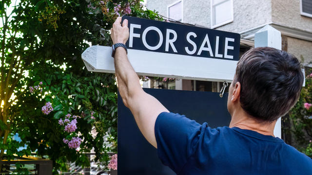Real Estate Agent Adjusts For Sale Sign in Front Yard 
