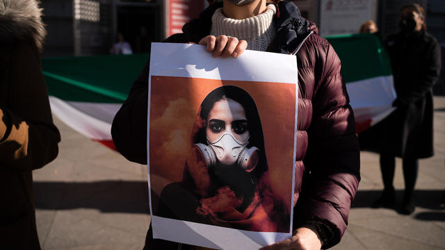 A woman holds a placard with a drawing of a girl wearing gas 
