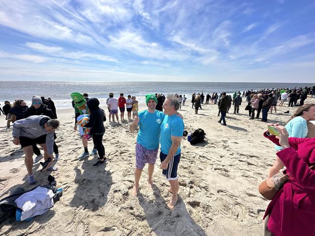 Polar Plunge in Cape may showing tow people arm in arm; one person shows thumbs up into the camera 