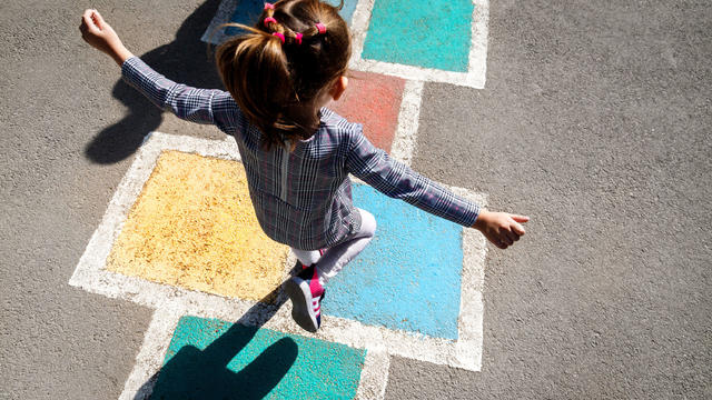 Kid girl 5 y.o. playing hopscotch on playground outdoors 