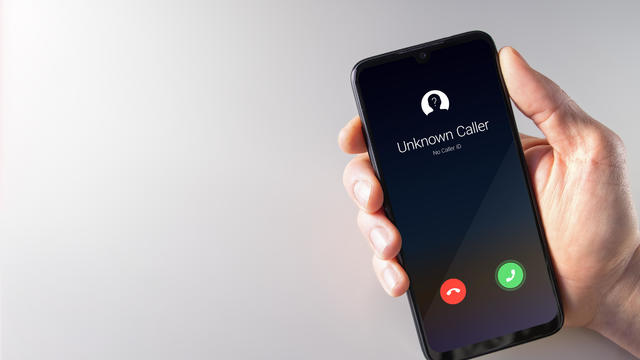Male hand holding a smartphone with unknown caller displayed on screen 