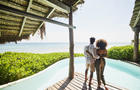 Wide shot rear view of couple standing poolside at luxury tropical beachfront villa looking at view 