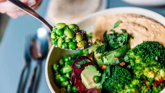 Eating vegan bowl with edamame beans, broccoli, avocado, beetroot, hummus and nuts 