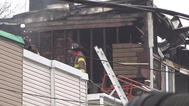 Firefighters stand on the roof of a building next to a home severely damaged by fire. 