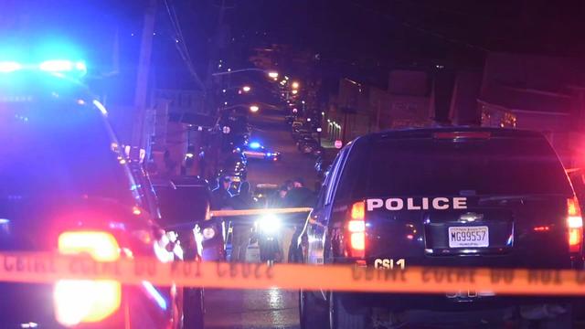 Multiple police vehicles parked on a street blocked off by crime scene tape at night. 