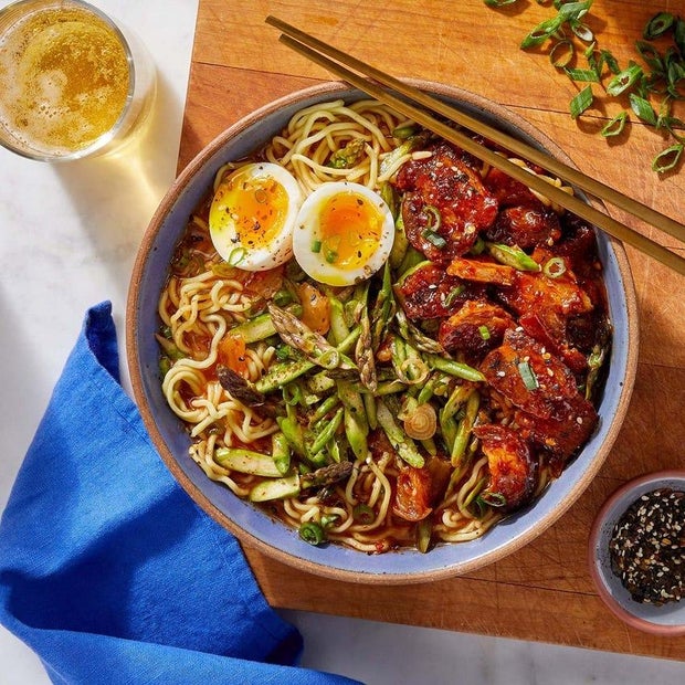 Soy-miso pork belly and kimchi ramen with soft-boiled eggs and furikake, pictured with chopsticks on a cutting board next to sliced scallions and furikake seasoning