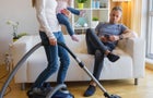 Woman with small child doing housekeeping while man sitting in couch 