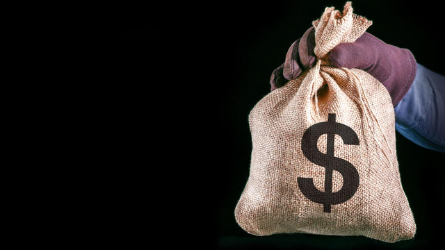Money bag with US dollar sign. Man hand with money bag on black background with copy space. Bank robber. 