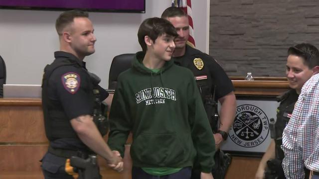 A teenager shakes the hand of a police officer who helped save him while standing next to two other officers. 