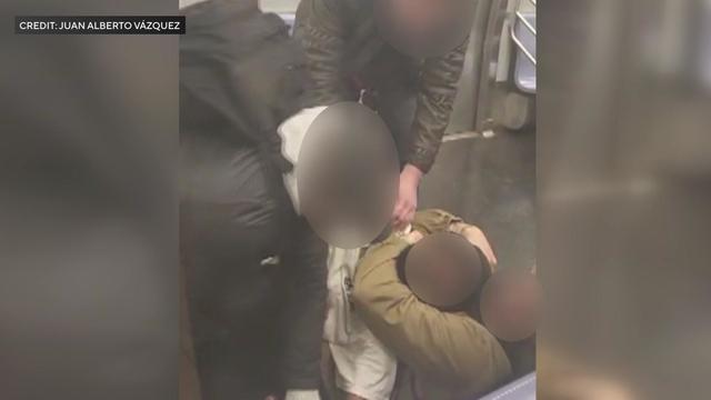A video shows one man holding another man in a chokehold on the floor of a subway car while two other individuals help restrain the man in the chokehold. 