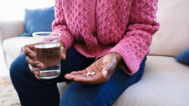 Woman Holds Capsules and Glass of Water 