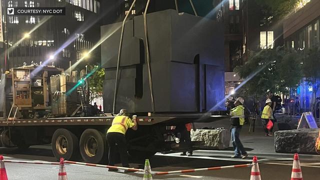 The Alamo Cube being loaded by a crane onto the back of a flatbed truck. 